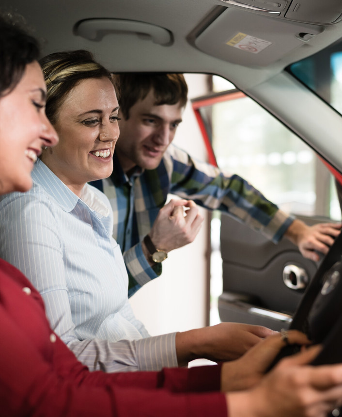 A dealer shows the inside of a car to a smiling woman and man
