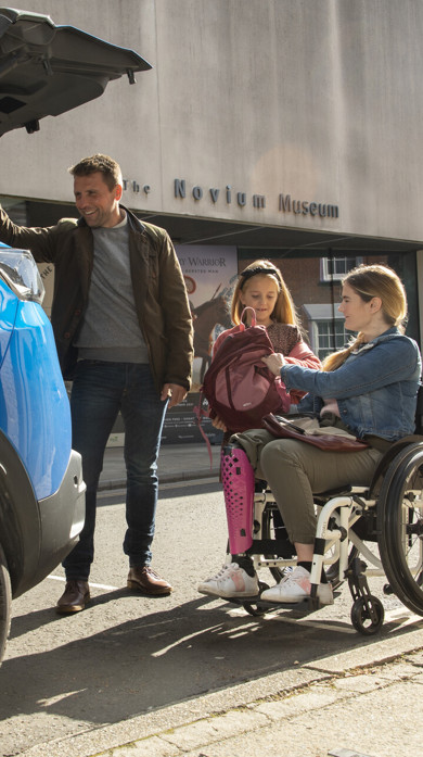 Man helping a woman in a wheelchair and a young girl unpack a car boot